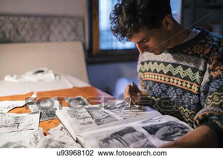 Stock Image - Male artist drawing in sketchbook at desk in artists studio. Fotosearch