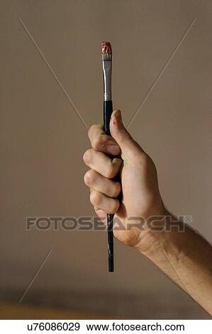 Stock Photo - Male artist holding paintbrush in artists studio, close up of hand. Fotosearch