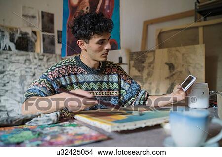 Male artist looking at smartphone while painting canvas in artists studio View Large Photo Image Picture - Male artist looking at smartphone while painting canvas in artists studio. Fotosearch