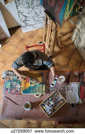 Stock Photo - Male artist looking at smartphone while painting canvas in artists studio, overhead view. Fotosearch