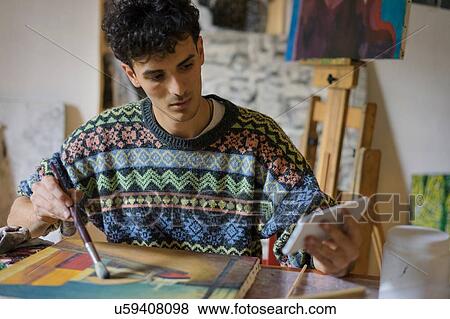 Male artist looking at smartphone while painting canvas in artists studio View Large Photo Image Stock Photo - Male artist looking at smartphone while painting canvas in artists studio. Fotosearch