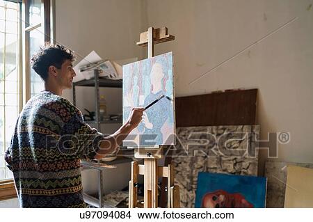 Picture - Male artist painting canvas at easel in artists studio. Fotosearch