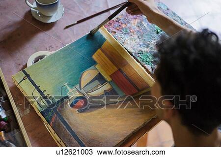 Stock Image - Male artist painting canvas in artists studio, over shoulder view. Fotosearch