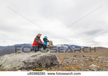 Stock Photography - Male hiker with son building cairn in mountain landscape, Jotunheimen National Park, Lom, Oppland, Norway. Fotosearch