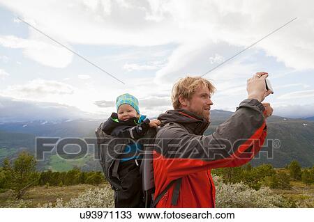 Stock Image - Male hiker with son photographing mountain landscape, Jotunheimen National Park, Lom, Oppland, Norway. Fotosearch