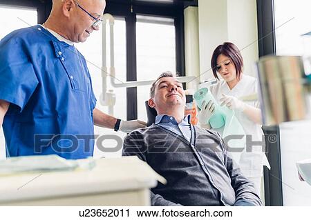 Male patient in dentist chair, dentist standing beside him View Large Photo Image Stock Image - Male patient in dentist chair, dentist standing beside him. Fotosearch