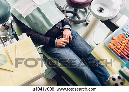 Stock Photo - Male patient in dentist chair, mid section, elevated view. Fotosearch