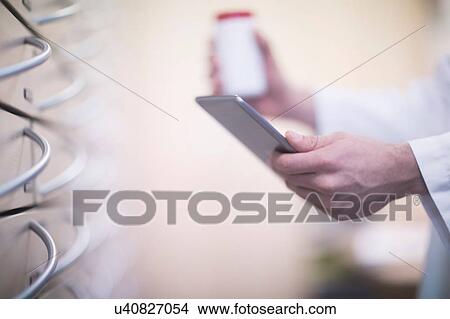 Picture - Male pharmacist holding pill bottle and digital tablet in pharmacy, close up of hand. Fotosearch