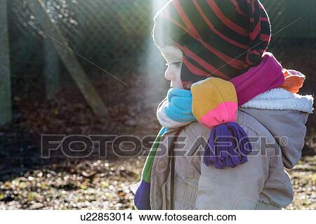 Picture - Male toddler in knit hat and scarf looking down in park. Fotosearch
