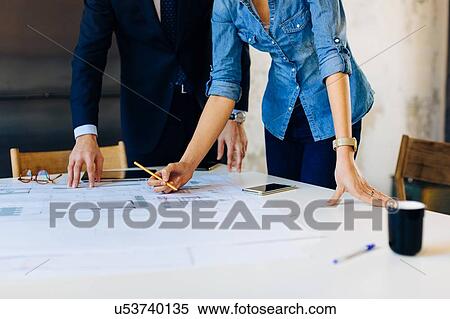 Man and woman in meeting, looking at blueprints, mid section View Large Photo Image Stock Photography - Man and woman in meeting, looking at blueprints, mid section. Fotosearch