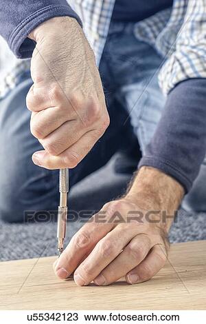 Stock Image - Man assembling furniture at home, hand with screwdriver.. Fotosearch