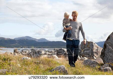 Stock Image - Man carrying son by fjord, Aure, More og Romsdal, Norway. Fotosearch