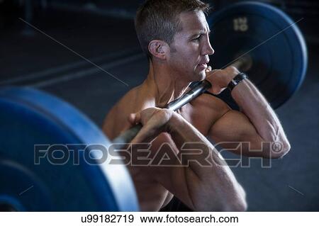 Stock Photo - Man exercising in gym, using barbell, front squat position. Fotosearch
