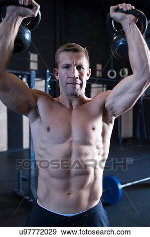 Man exercising in gymnasium, lifting kettlebells View Large Photo Image Stock Photo - Man exercising in gymnasium, lifting kettlebells. Fotosearch
