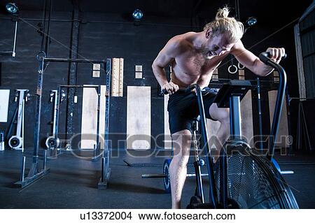 Picture - Man exercising in gymnasium, using air resistance exercise bike. Fotosearch