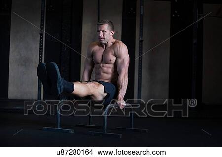 Picture - Man exercising in gymnasium, using parallel bars, in L-sit hold. Fotosearch