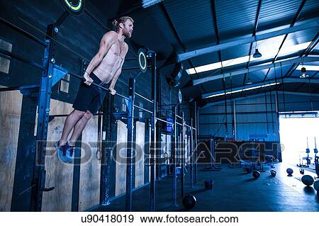Stock Photo - Man exercising in gymnasium, using pull up bars. Fotosearch