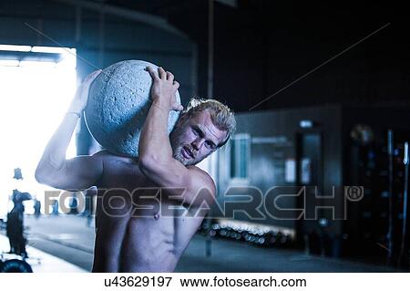 Man exercising in gymnasium, using atlas stone View Large Photo Image Stock Photo - Man exercising in gymnasium, using atlas stone. Fotosearch