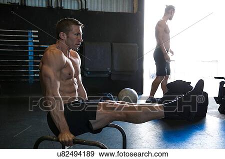 Stock Photo - Man exercising in gymnasium, using parallel bars, in L-sit position. Fotosearch