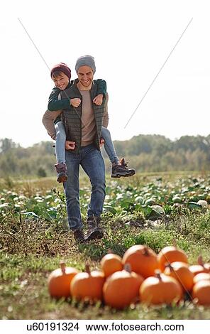 Picture - Man giving son piggyback ride in field at pumpkin patch. Fotosearch