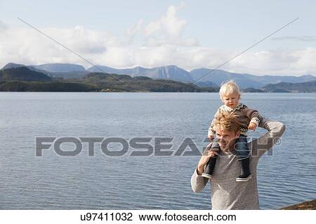 Stock Image - Man giving son shoulder ride by fjord, Aure, More og Romsdal, Norway. Fotosearch