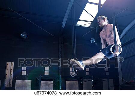 Stock Photo - Man in gymnasium, balancing on gymnastic rings. Fotosearch