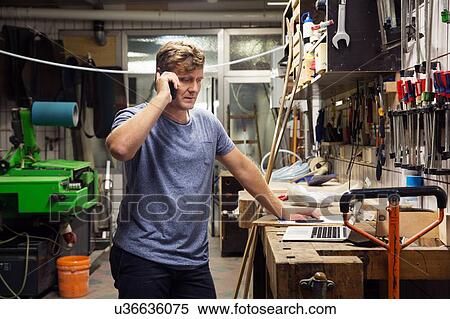 Man in workshop, using smartphone, looking at laptop View Large Photo Image Stock Photography - Man in workshop, using smartphone, looking at laptop. Fotosearch
