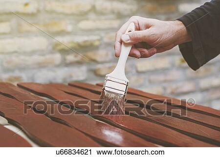 Stock Image - Man painting wooden pickets for hash fence.. Fotosearch
