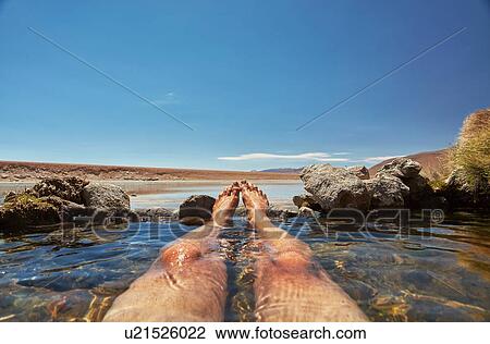 Stock Image - Man relaxing in water pool, low section, Salar de Chiguana, Chiguana, Potosi, Bolivia, South America. Fotosearch