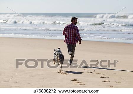 Stock Image - Man running with dog on beach. Fotosearch