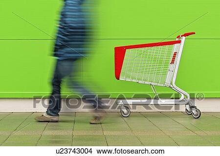 Picture - Man walking by empty shopping trolley.. Fotosearch