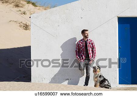 Stock Photo - Man with dog leaning against wall at beach. Fotosearch