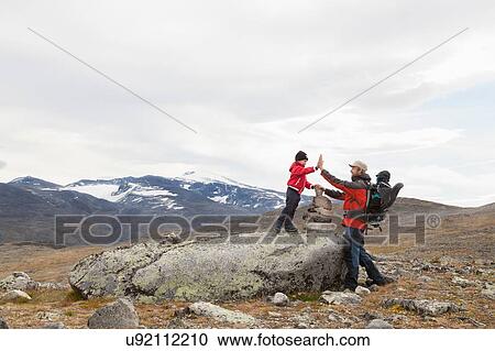 Stock Image - Man with sons high fiving over cairn in mountain landscape, Jotunheimen National Park, Lom, Oppland, Norway. Fotosearch