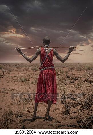 Picture - Masai man with traditional dress watching stormy clouds over the savannah, Amboseli, Rift Valley, Kenya. Fotosearch