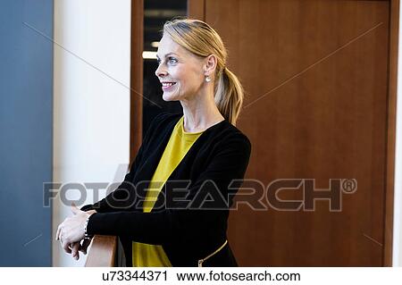 Stock Image - Mature businesswoman looking out over office atrium. Fotosearch