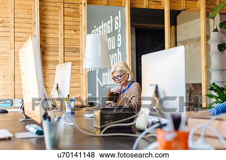 Mature businesswoman sitting at desk, working View Large Photo Image Stock Photo - Mature businesswoman sitting at desk, working. Fotosearch