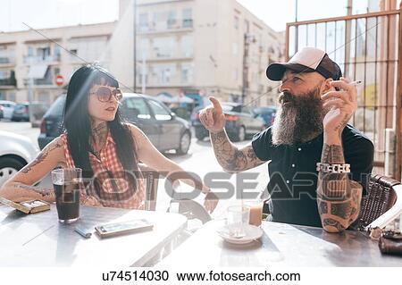 Stock Image - Mature hipster couple chatting at sidewalk cafe, Valencia, Spain. Fotosearch