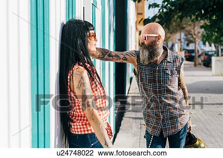 Stock Image - Mature hipster couple face to face on sidewalk. Fotosearch