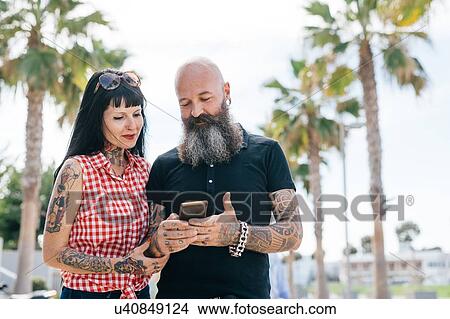 Picture - Mature hipster couple in park looking at smartphone, Valencia, Spain. Fotosearch