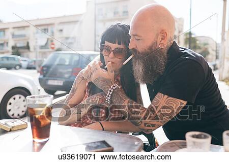 Stock Image - Mature hipster couple lighting cigarette at sidewalk cafe, Valencia, Spain. Fotosearch