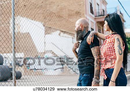 Stock Photo - Mature hipster couple looking beyond wire fence. Fotosearch