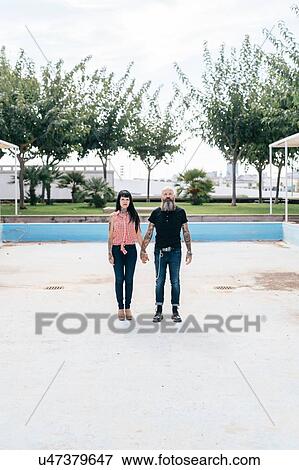 Stock Photo - Mature hipster couple standing in empty swimming pool, portrait, Valencia, Spain. Fotosearch