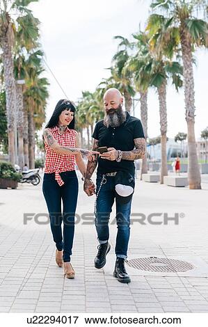 Mature hipster couple strolling while looking at smartphone on sidewalk, Valencia, Spain View Large Photo Image Stock Photo - Mature hipster couple strolling while looking at smartphone on sidewalk, Valencia, Spain. Fotosearch
