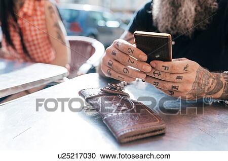 Mature hipster man using smartphone at sidewalk cafe, close up of tattooed hand View Large Photo Image Stock Image - Mature hipster man using smartphone at sidewalk cafe, close up of tattooed hand. Fotosearch