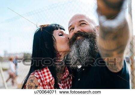 Stock Image - Mature hipster woman kissing boyfriend while taking selfie. Fotosearch