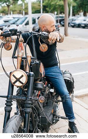 Stock Photo - Mature male hipster astride motorcycle, looking over his shoulder. Fotosearch