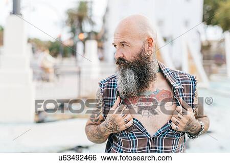 Stock Photograph - Mature male hipster revealing tattooed chest. Fotosearch