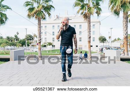 Stock Photo - Mature male hipster smoking cigarette and strolling in city, Valencia, Spain. Fotosearch