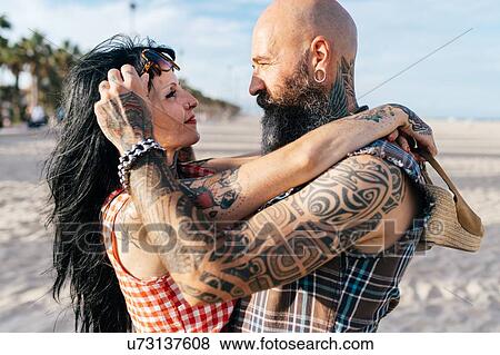 Stock Photo - Mature tattooed hipster couple face to face on beach, Valencia, Spain. Fotosearch