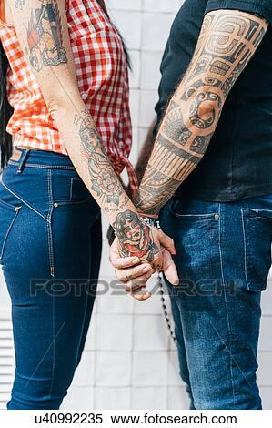 Stock Photography - Mature tattooed hipster couple holding hands, mid section. Fotosearch